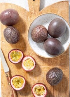 several pieces of passion fruit sit on a wood cutting board with a knife