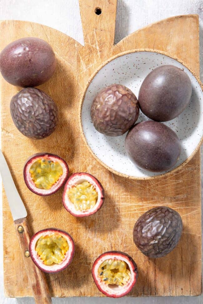 Several passion fruit on a wooden cutting board with a knife.