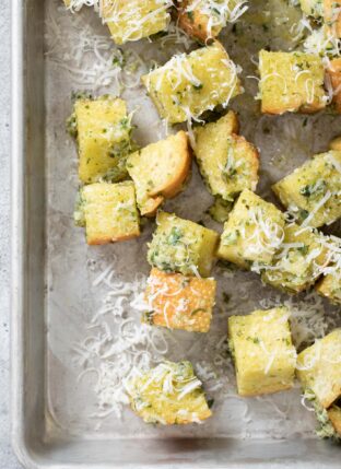 An aluminum cookie sheet filled with basil pesto croutons (Italian croutons).