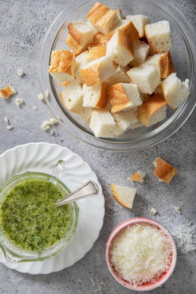a clear bowl filled with cut bread cubes; a bowl with pesto sits next to the bowl of bread cubes