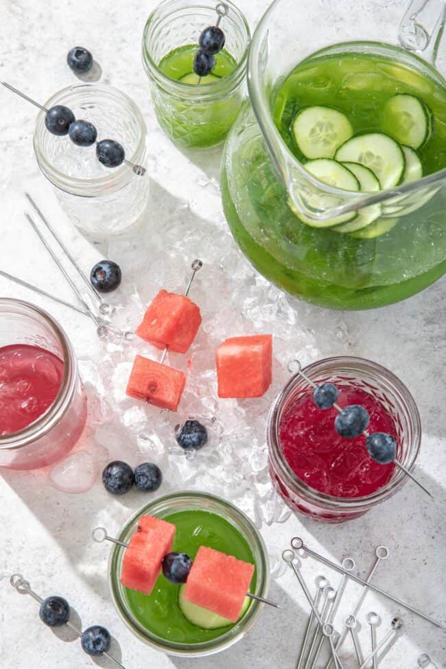 A clear glass pitcher filled with green juice and clear glasses filled with red and green juice 