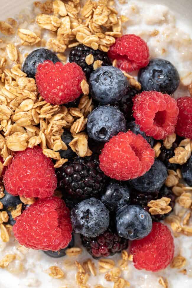 A white bowl filled with oatmeal, granola and mixed berries