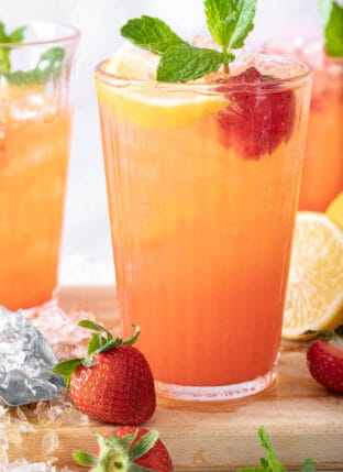 3 glasses filled with strawberry lemonade and garnished with strawberries, lemon slices and mint sprigs