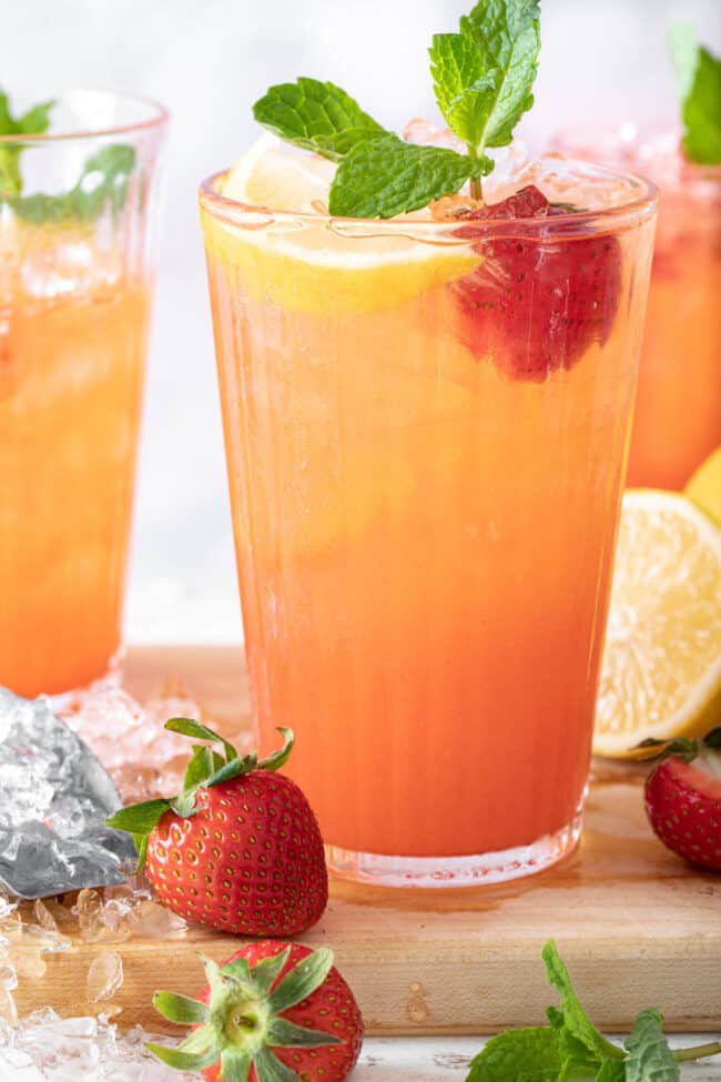 3 clear glasses filled with strawberry lemonade. A strawberry, slice of lemon and sprig of mint garnishes the drinks.