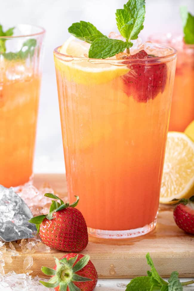 3 clear glasses filled with strawberry lemonade. A strawberry, slice of lemon and sprig of mint garnishes the drinks