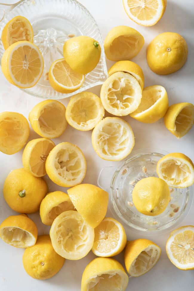 Two glass juicers sit next to many squeezed lemon halves.