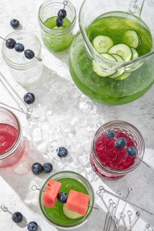 A clear glass pitcher filled with green juice and clear glasses filled with red and green juice to measure how many cups in a gallon