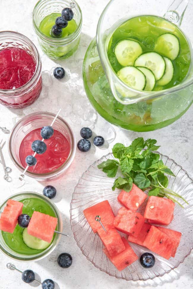 A clear glass pitcher filled with green juice and clear glasses filled with red and green juice to measure how many cups in a gallon