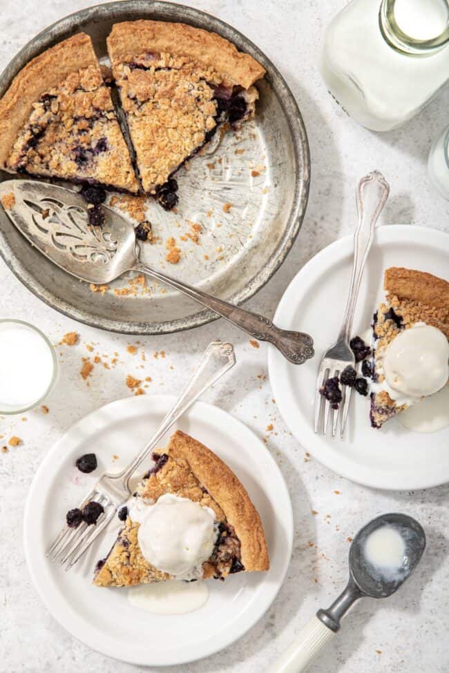 two slices of pie in a pie tin next to two white plates with pie and a scoop of vanilla ice cream on top