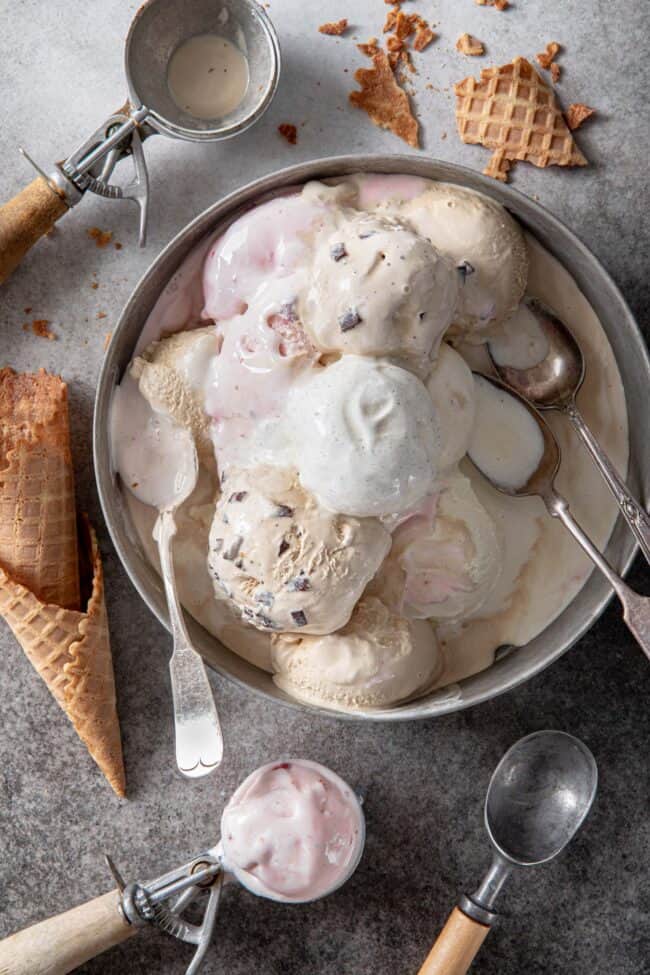 an aluminum cake pan filled with scoops of ice cream and 3 spoons. Ice cream scoops filled with ice cream sit next to the pan.
