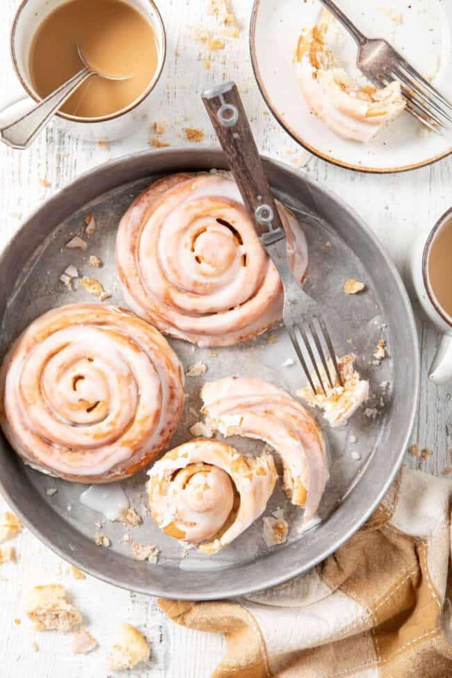 two cinnamon rolls sit in a cake tin with a fork - for how to measure how many tablespoons in a quarter cup