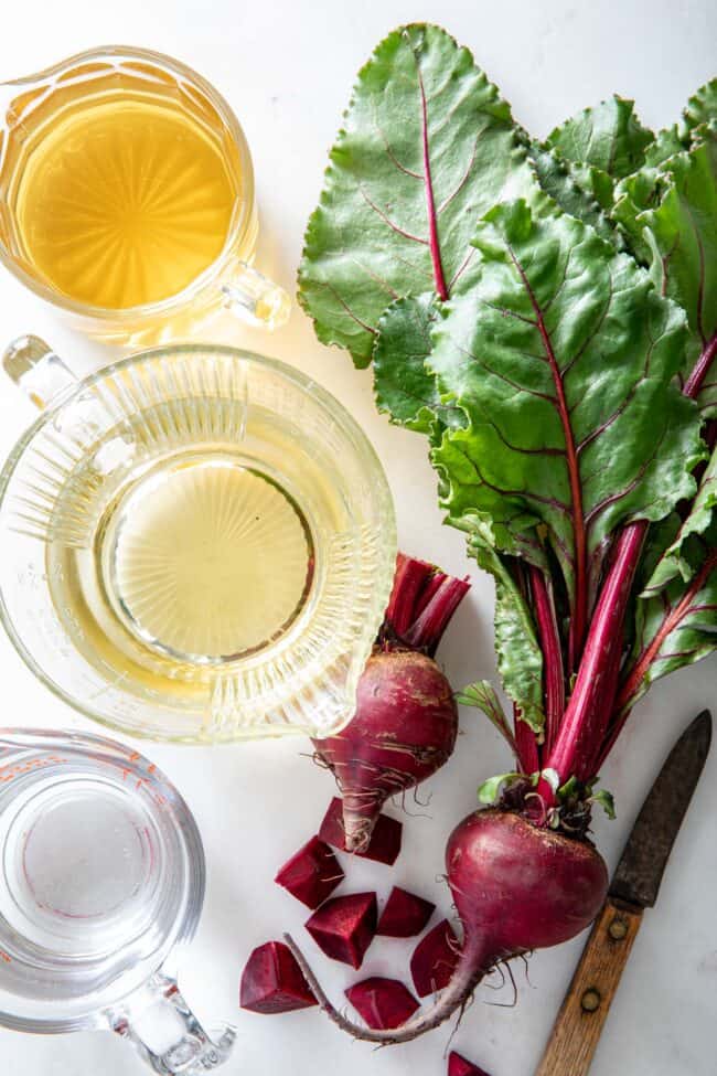 Raw beets with a knife. Three glass measuring cups filled with apple juice, white grape juice and water to make beet juice