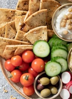 A plate filled with cherry tomatoes, cucumber slices, olives, and homemade pita chips.