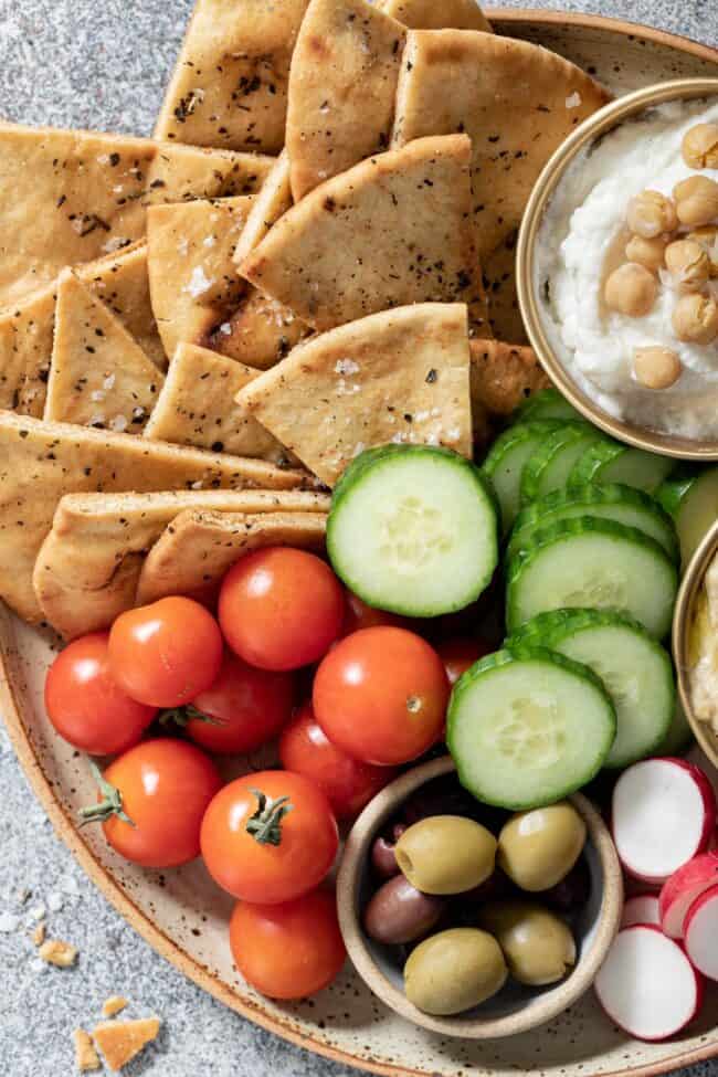 A plate filled with cherry tomatoes, cucumber slices, olives, and homemade pita chips.