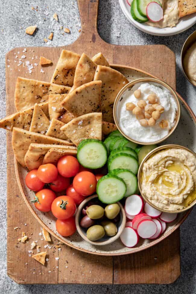 a plate filled with cherry tomatoes, cucumber slices, olives, hummus and garlic dip 