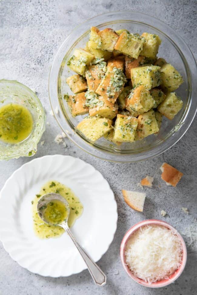 a clear glass bowl filled with bread cubes tossed in basil pesto
