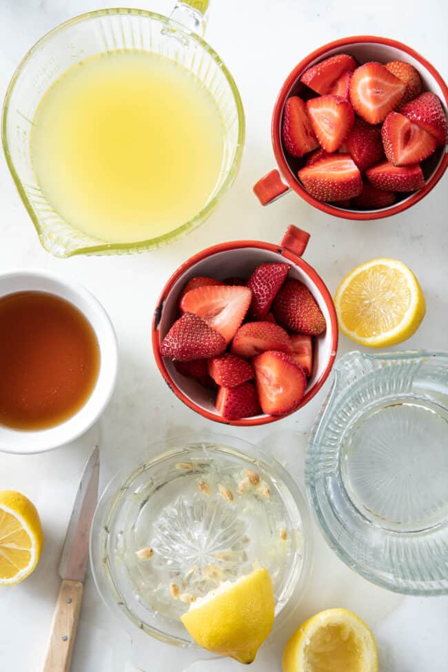 A glass measuring cup filled with lemon juice and one filled with water. Two cups filled with cut strawberries.