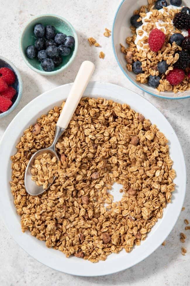 A white dish filled with granola. A bowl filled with yogurt and granola sits next to the dish.