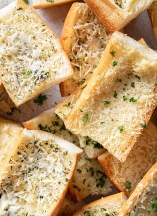 Cut pieces of garlic bread are scattered on a baking sheet.