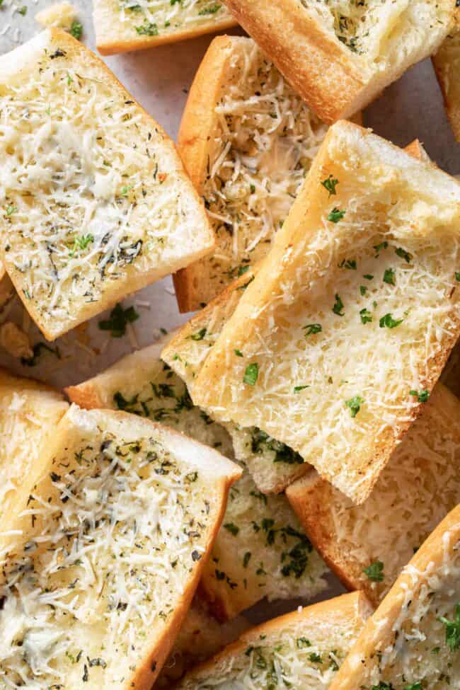 Cut pieces of garlic bread are scattered on a baking sheet.