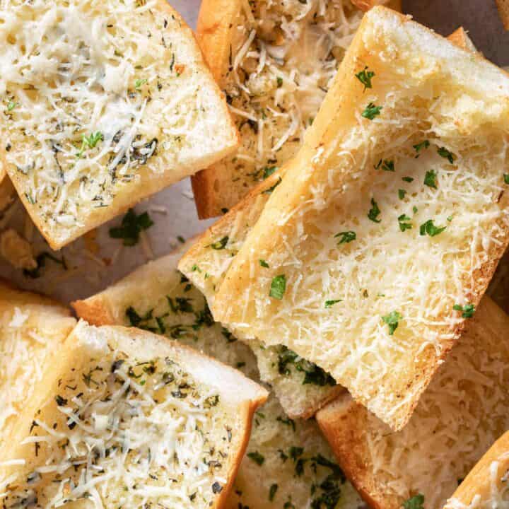 Cut pieces of garlic bread are scattered on a baking sheet.