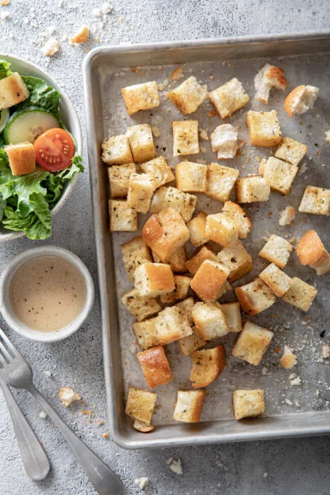 a cookie sheet filled with homemade croutons. A green salad and fork sits next to the cookie sheet.