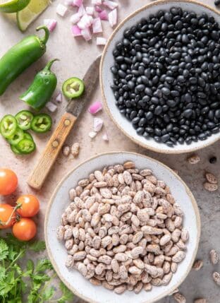 Two bowls filled with beans - one filled with dried black beans and the other with dried pinto beans.