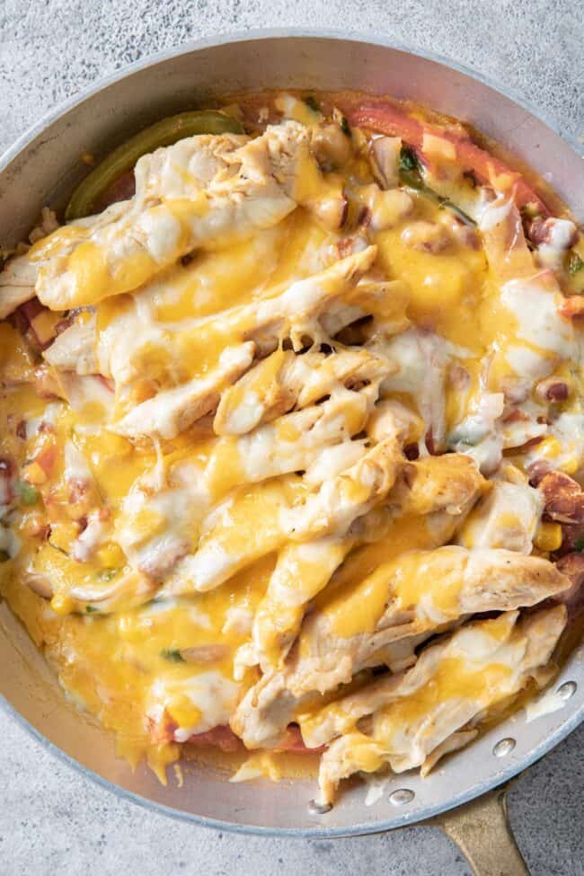 a metal skillet filled with cooked poultry, pinto beans, onion and bell pepper topped with melted cheese.