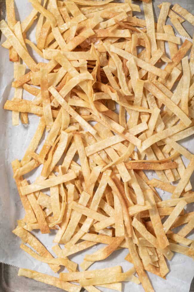 Homemade tortilla strips scattered on a cookie sheet.