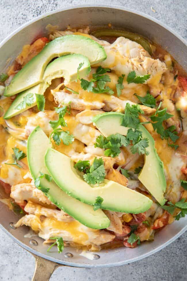 a metal skillet filled with chicken fajita casserole and avocado slices. 