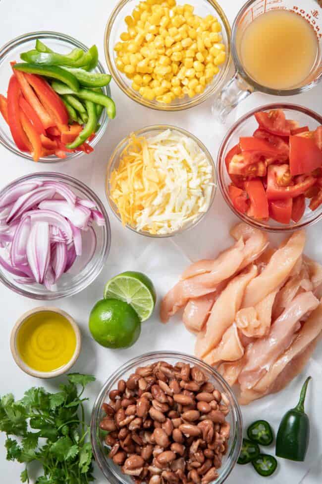 clear glass bowls filled with sliced bell pepper, onions, grated cheese, pinto beans, tomato and corn