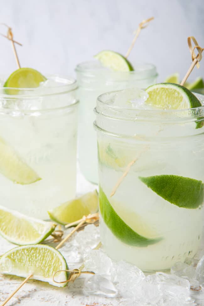 Three clear drinking glasses filled with limeade, ice and slices of limes.