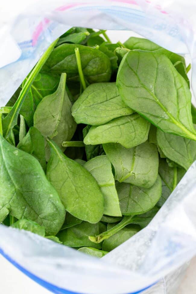 A freezer bag filled with frozen spinach leaves.