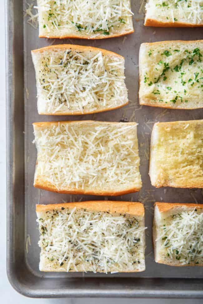 Several slices of baguette on a baking sheet. They're overed with grated Parmesan cheese.