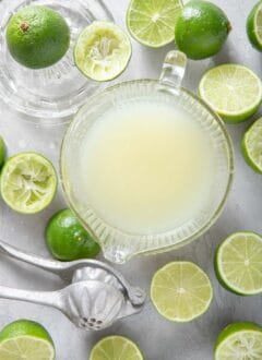 Many limes cut in half sit next to a glass measuring cup filled with lime juice for how much juice in a lime