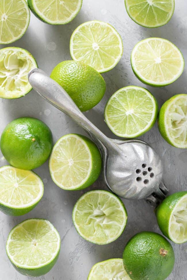 Many citrus fruits cut in half sit next to a metal hand juicer 