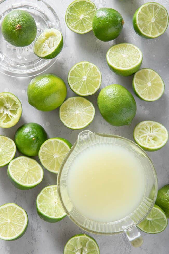 many limes cut in half sit next to a glass measuring cup filled with lime juice for how much juice in one lime