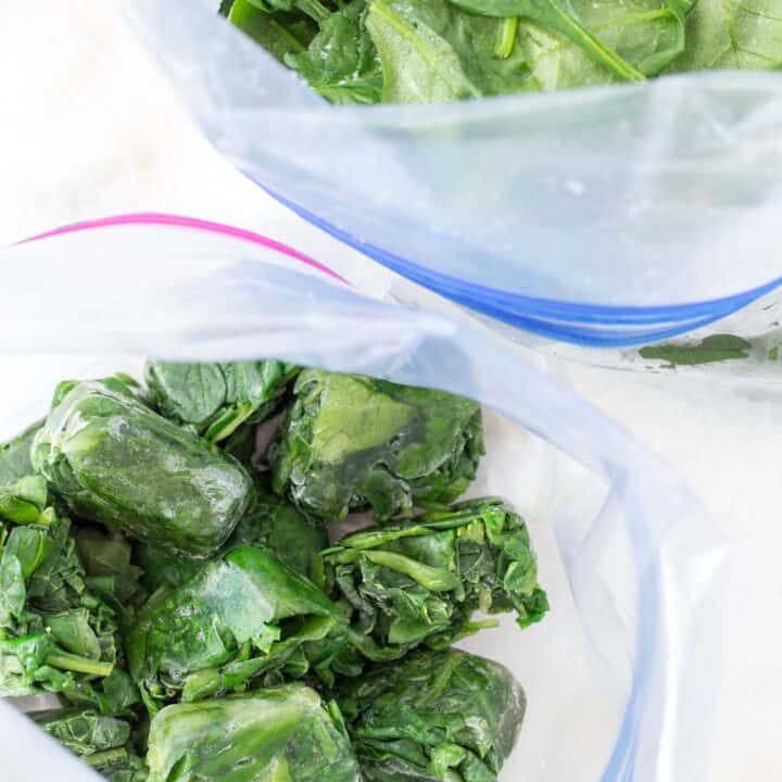 A white ice cube tray filled with green vegetable leaves.