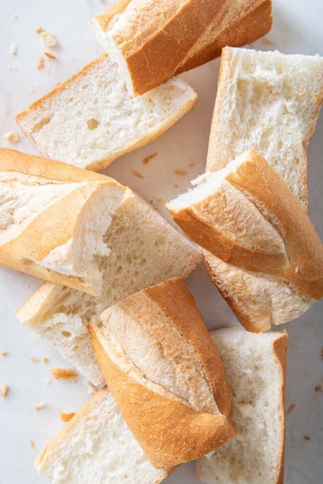Several sliced pieces of baguette are scattered on a white cutting board.
