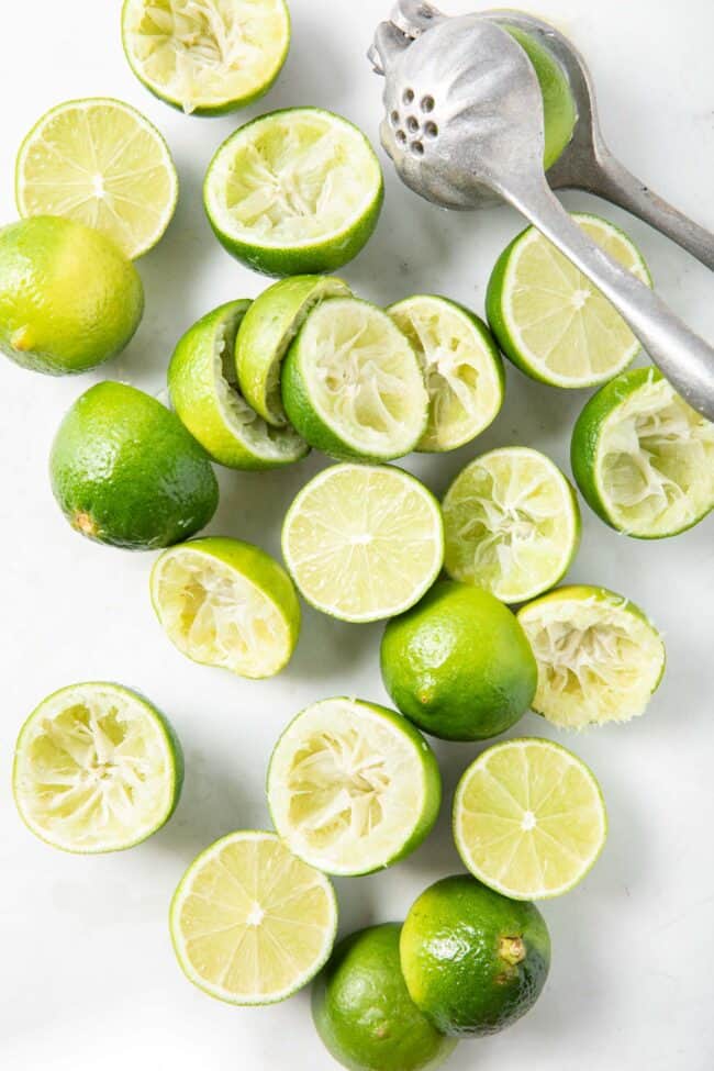 Many limes cut in half - some juiced sitting near the pile is a metal hand held juicer.