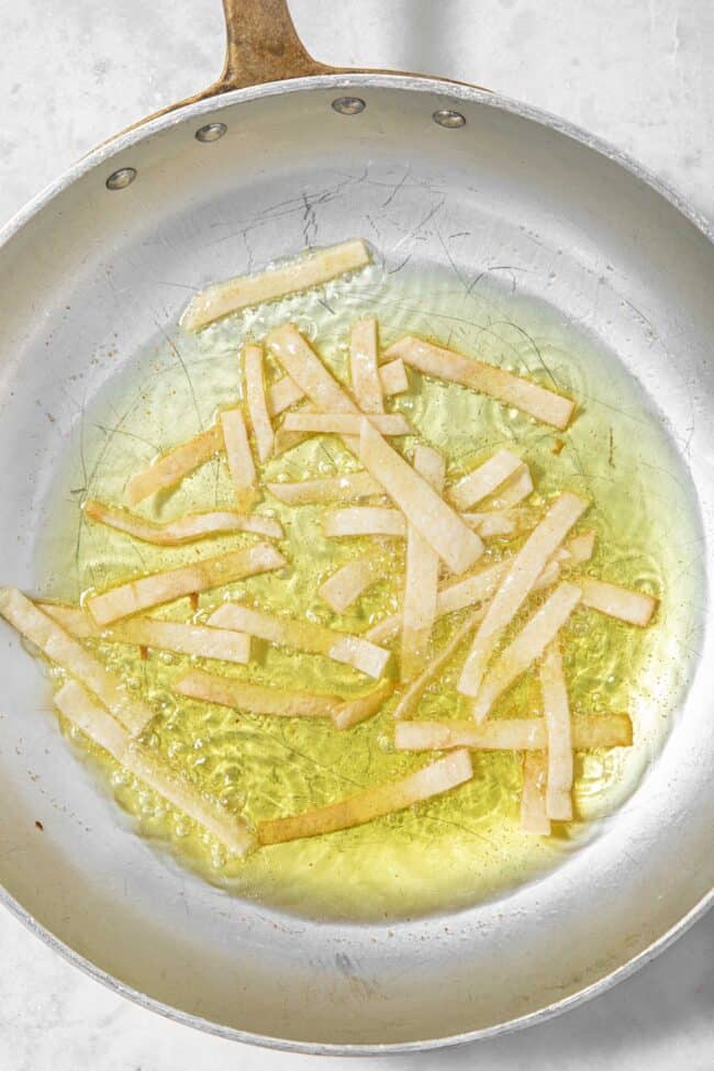 Crispy chips frying in a pan with oil. The oil is bubbling.