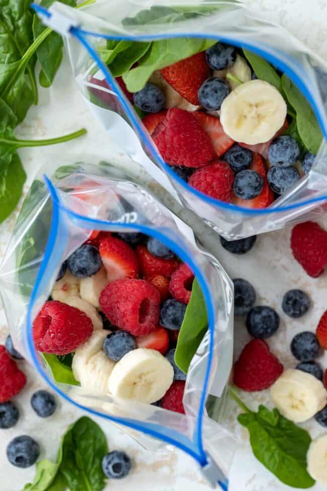 Two freezer bags filled with greens, banana slices, strawberries, raspberries and blueberries.