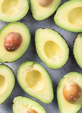 Several avocados sliced in half with their seeds.