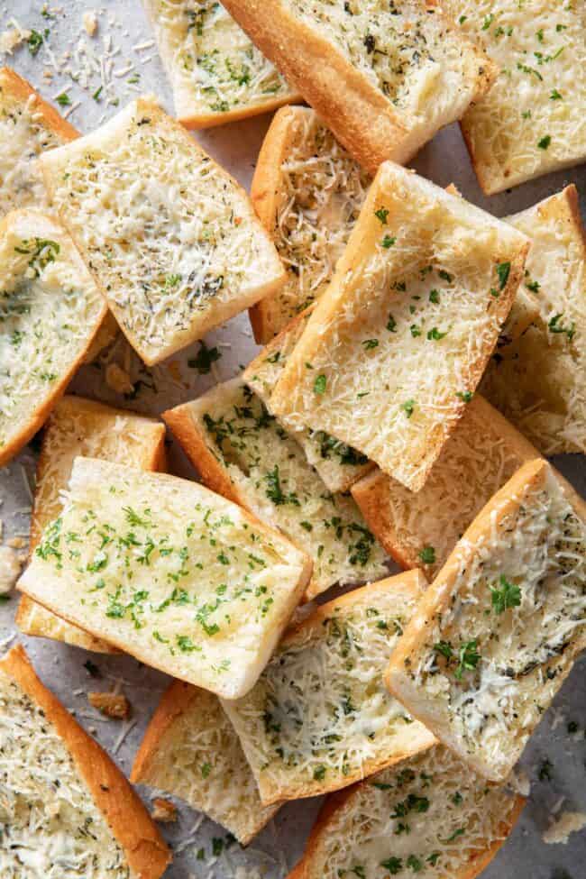 Several slices of garlic bread scattered on a cookie sheet.