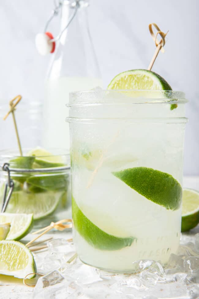 A clear drinking glass filled with limeade, ice and lime slices. 