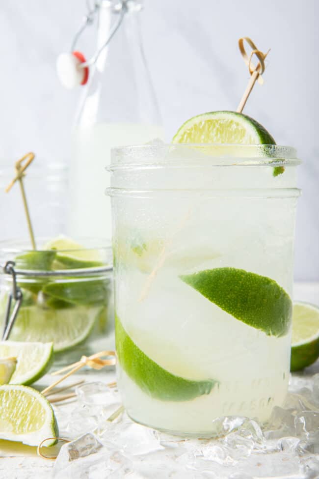 A clear drinking glass filled with limeade, ice and lime slices. 
