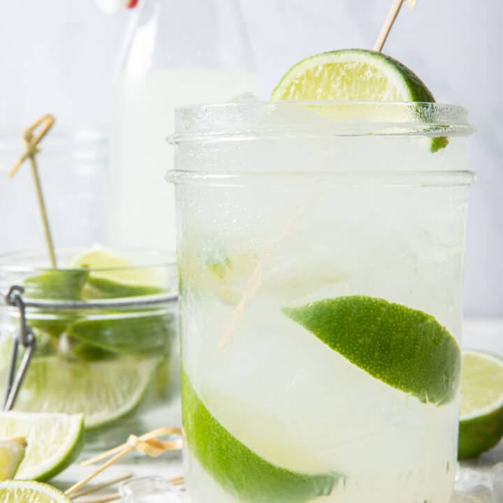 A clear drinking glass filled with limeade, ice and lime slices