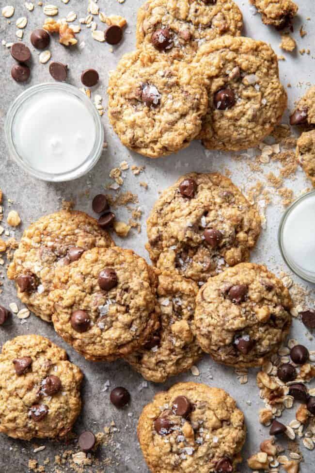 Oatmeal chocolate chip cookies scattered on a table with two glasses of milk