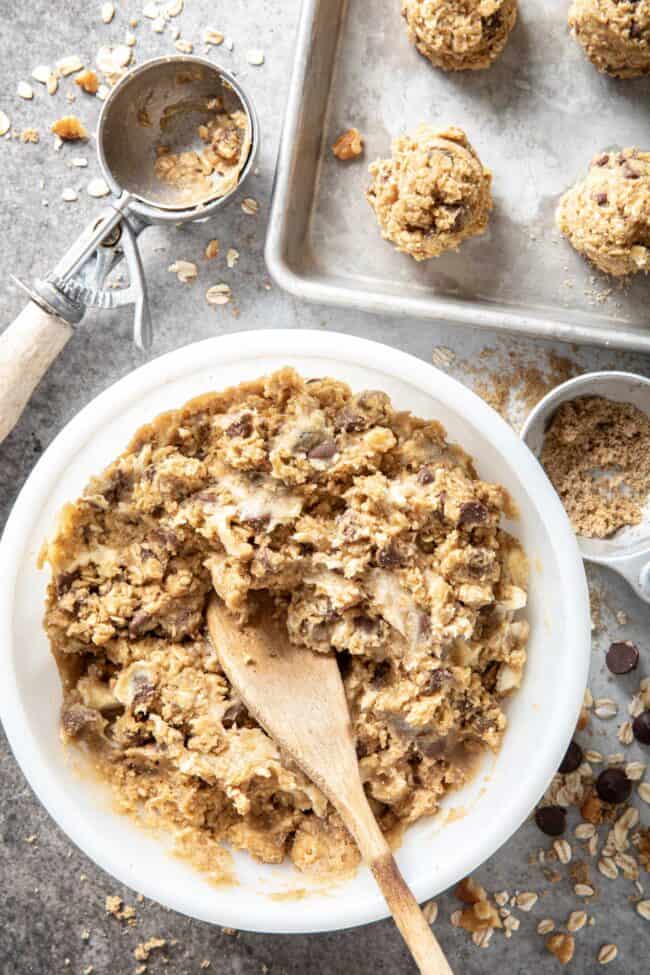 A white bowl filled with oatmeal chocolate chip cookie dough. A cookie sheet sits next to the bowl with balls of cookie dough. For how many ounces in a pound conversions.