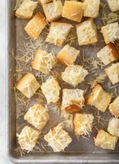 A cookie sheet filled with bread cubes tossed in butter and Parmesan cheese for Parmesan croutons.